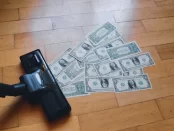 A vacuum sucking up money fanned out across a wood floor.